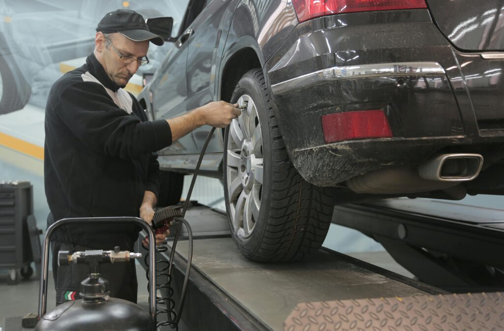 A male mechanic checks tire pressure on a vehicle in a workshop setting, showcasing automotive expertise.
