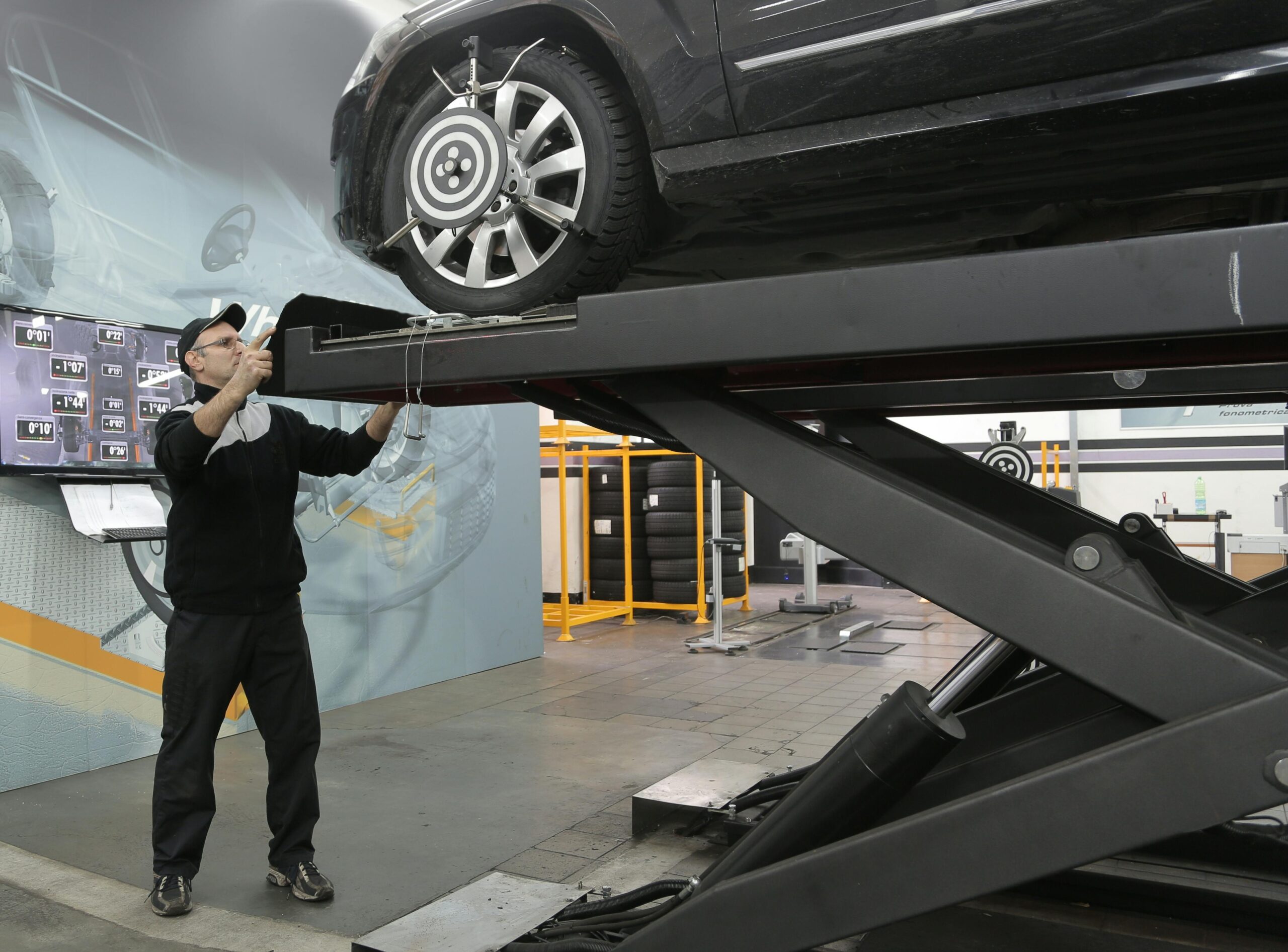 Mechanic carefully examining car on hydraulic lift in automotive workshop, ensuring safety and performance.