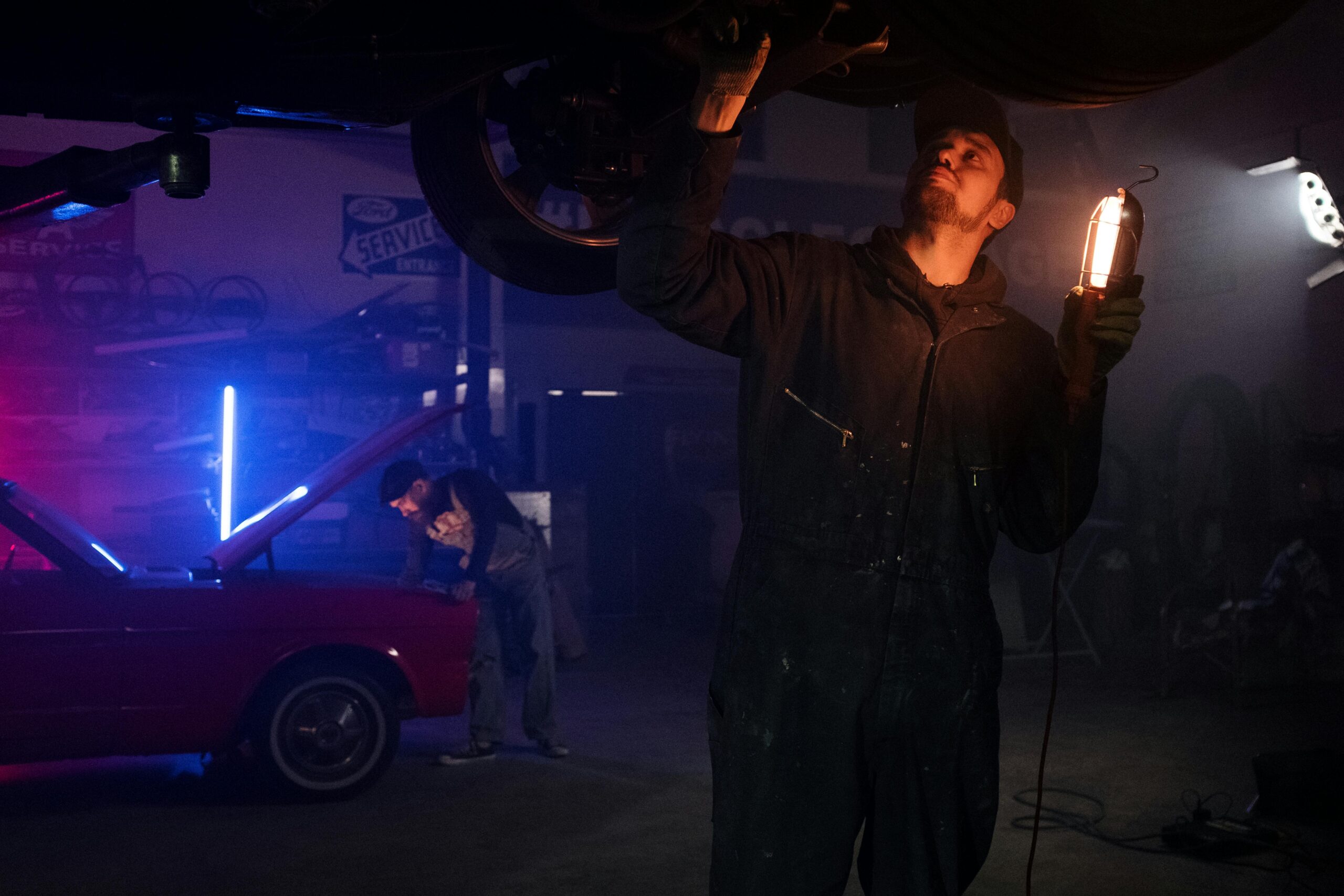 Mechanic working on a vehicle under neon lights in a dark garage, showcasing automotive repair skills.